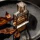 Luxury perfume bottle with amber liquid and dried leaves, symbolizing long-lasting scents like Parfum and Eau de Parfum.