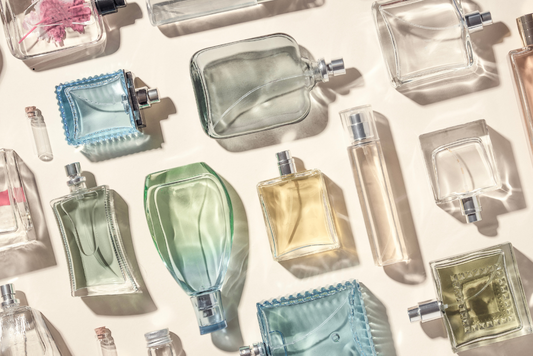 Eau de parfum and perfume bottles in assorted shapes and colors, flat lay on beige background.