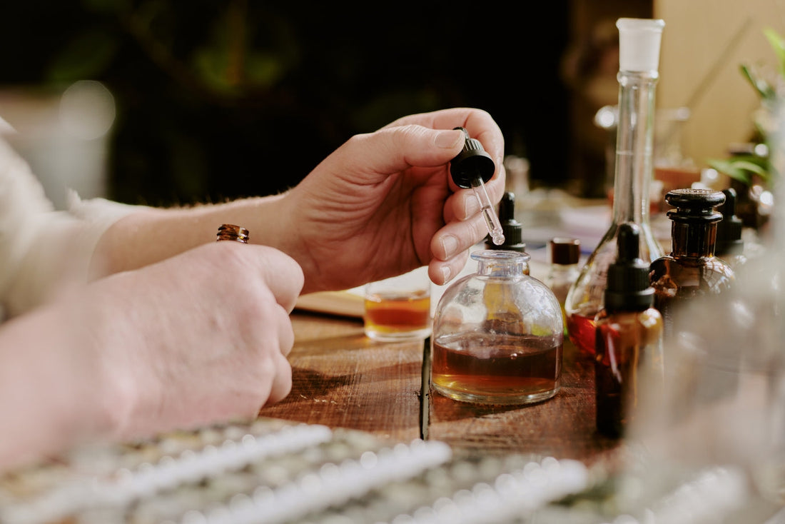 Close-up of hands using a dropper to blend fragrance oils into a small glass perfume bottle on a wooden table