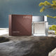 Calvin Klein Euphoria Men cologne bottle on a rocky surface with a lake and trees in the background.