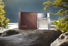 Calvin Klein Euphoria Men cologne bottle on a rocky surface with a lake and trees in the background.