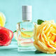 Luxury perfume bottle with golden liquid, surrounded by yellow and red roses, on a blue background.