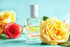 Luxury perfume bottle with golden liquid, surrounded by yellow and red roses, on a blue background.