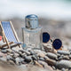 Perfume bottle with sunglasses on a sunny pebble beach