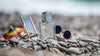 Perfume bottle with sunglasses on a sunny pebble beach