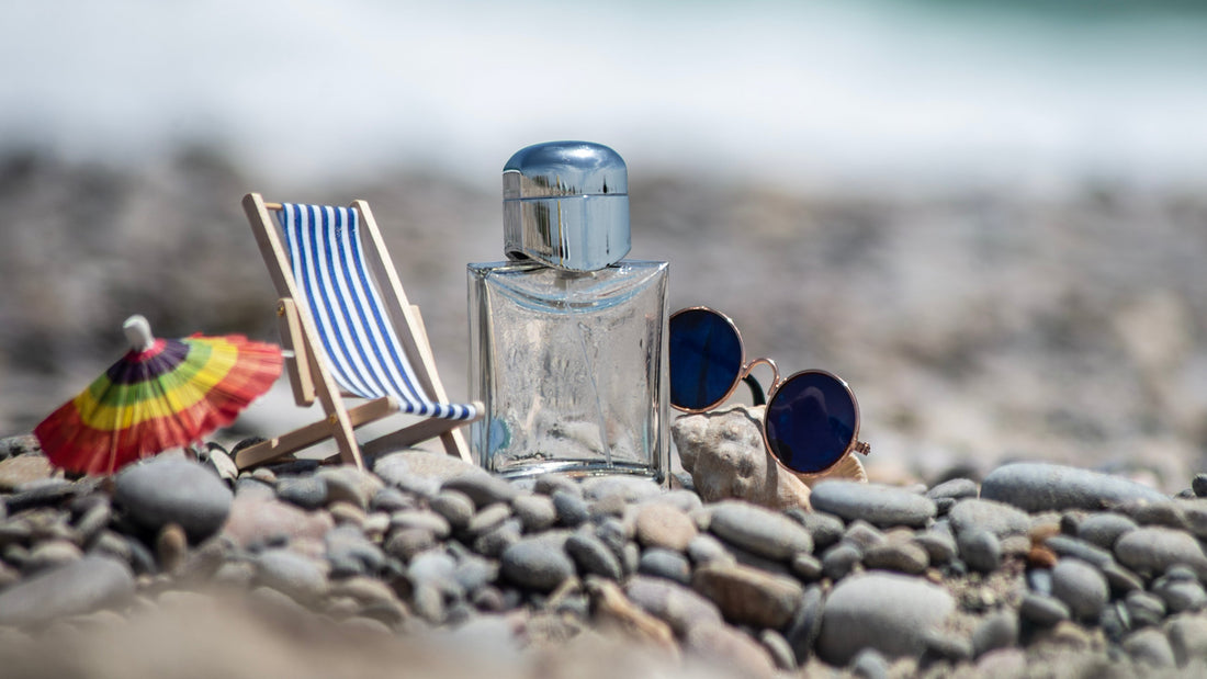 Perfume bottle with sunglasses on a sunny pebble beach